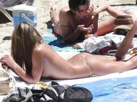 She Sits Nude on the Sand Between Ocean Waves and Cliffs
