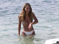 She Sits Nude on the Sand Between Ocean Waves and Cliffs
