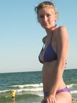 She Sits Nude on the Sand Between Ocean Waves and Cliffs