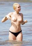 She Sits Nude on the Sand Between Ocean Waves and Cliffs