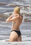 She Sits Nude on the Sand Between Ocean Waves and Cliffs