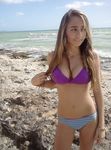 She Sits Nude on the Sand Between Ocean Waves and Cliffs