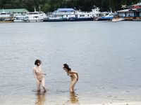 Dvě ženy klečí u břehu na písečné nudistické pláži