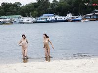 Dvě ženy klečí u břehu na písečné nudistické pláži