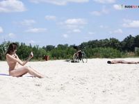 Dvě ženy klečí u břehu na písečné nudistické pláži