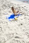 Bending Low to Pick Up a Purple Paddle and Pink Ball on Sand