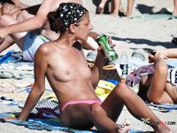 Single brunette is playing cards on the beach in the family nudist camp while showing her natural tits and getting tanned, not knowing that someone is watching