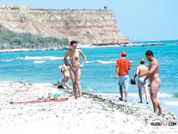 Multiple girls walk around or sit in the sand topless, with their amazing, natural breasts on display