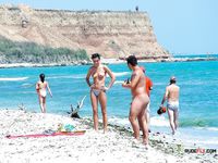 Multiple girls walk around or sit in the sand topless, with their amazing, natural breasts on display