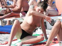This dazzling blonde sits on the rocky beach topless and enjoys her day, unaware she's being filmed
