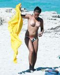 She sits in the sand topless and applies sunscreen on her slim body and large, natural breasts 2