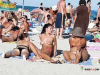 Attractive naturist girl seems so voluptuous as she sits naked at the beach and shows her gorgeous titties to everyone who passes next to her