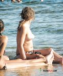 Drei oben-ohne Frauen spazieren an bunten Schirmen vorbei