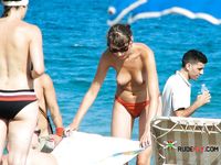 Drei oben-ohne Frauen spazieren an bunten Schirmen vorbei