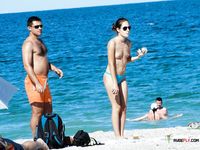 Brunette MILF with big tits is sitting on the beach joined by her husband as she spreads her legs wide to reveal her shaved pussy 2