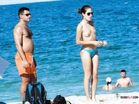 Brunette MILF with big tits is sitting on the beach joined by her husband as she spreads her legs wide to reveal her shaved pussy 2
