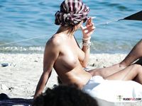 Brunette MILF with big tits is sitting on the beach joined by her husband as she spreads her legs wide to reveal her shaved pussy 2