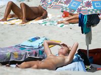 A sensual couple enjoys their day at the beach among a nudist colony while the sun heats their attractive, naked young bodies 2