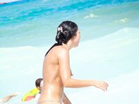 A breathtaking view of the coastline where a lady is seen relaxing in a natural, topless state.