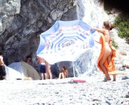 Nahý okamžik na skalnatém pobřeží s oranžovým ručníkem