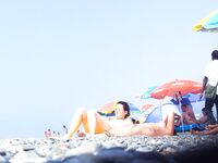 Nahý okamžik na skalnatém pobřeží s oranžovým ručníkem