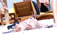 Topless on the Sand With Pink Bottoms and Straw Umbrellas Behind Her