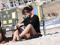 Adjusting a Sandal While Seated on the Beach Sand