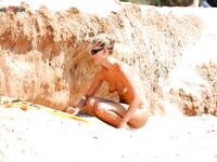 Adjusting Her Sunglasses Beside a Crouching Companion on a Nude Beach