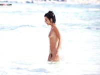 Adjusting Her Sunglasses Beside a Crouching Companion on a Nude Beach