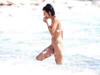Adjusting Her Sunglasses Beside a Crouching Companion on a Nude Beach