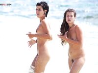 Adjusting Her Sunglasses Beside a Crouching Companion on a Nude Beach