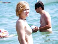 Two Nudists Share a White Towel Beside a Low Dune