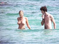 Two Naturists Pause Mid-Wade in Calm Shallow Sea Water