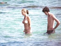 Two Naturists Pause Mid-Wade in Calm Shallow Sea Water