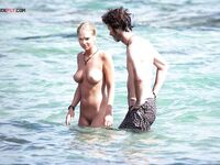 Two Naturists Pause Mid-Wade in Calm Shallow Sea Water