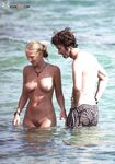 Two Naturists Pause Mid-Wade in Calm Shallow Sea Water