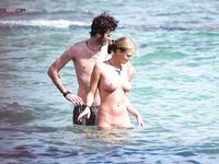 Two Naturists Pause Mid-Wade in Calm Shallow Sea Water