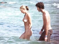 Two Naturists Pause Mid-Wade in Calm Shallow Sea Water