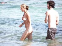 Two Naturists Pause Mid-Wade in Calm Shallow Sea Water