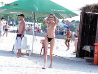 Zwarte bikinibroek onder een groene Tuborg-parasol aan een druk strand