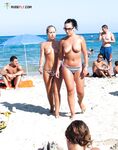 Two Nudists Near the Shoreline With a Bicycle on the Sand