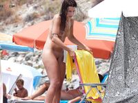 A lady enjoying a cold drink while sunbathing topless on the warm shore. 3