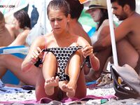 A lady enjoying a cold drink while sunbathing topless on the warm shore. 3