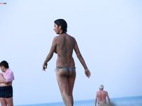 The natural light of the shore accentuating the beauty of a topless model on the sand.