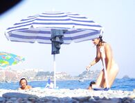 Two Women Talk Beside Calm Water on a Rocky Nudist Shore