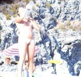 Two Women Talk Beside Calm Water on a Rocky Nudist Shore
