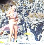 Two Women Talk Beside Calm Water on a Rocky Nudist Shore