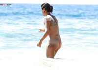 Fraîchement sortie des vagues, tatouages et sable collé à la peau sur le rivage