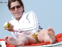 Brushing Sand From Her Raised Foot on a Red Beach Towel
