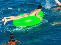 Three Nudists Laugh Together on a Bright Green Pool Float